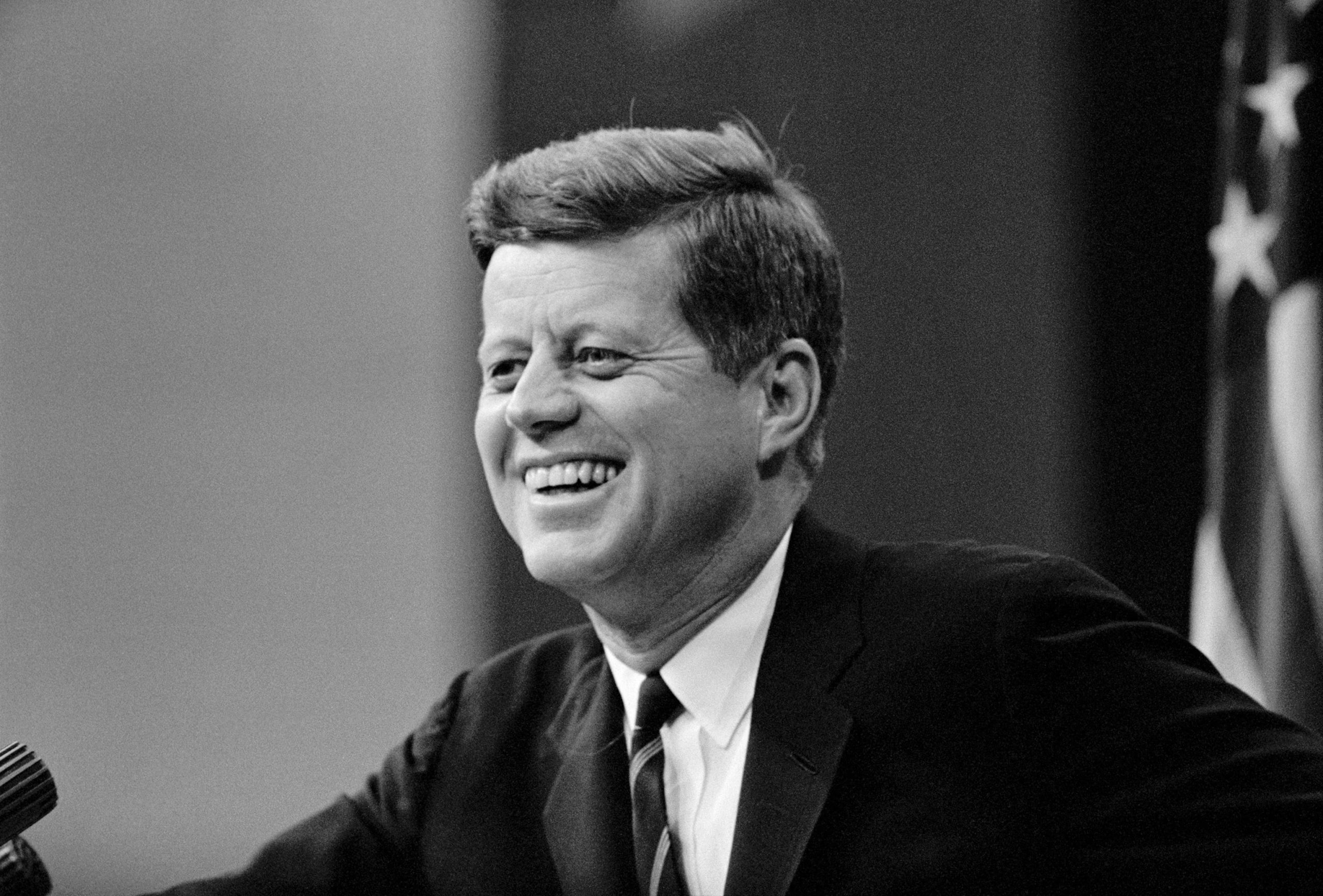 O ex-presidente dos Estados Unidos John F. Kennedy em foto em preto e branco, sorrindo, de perfil