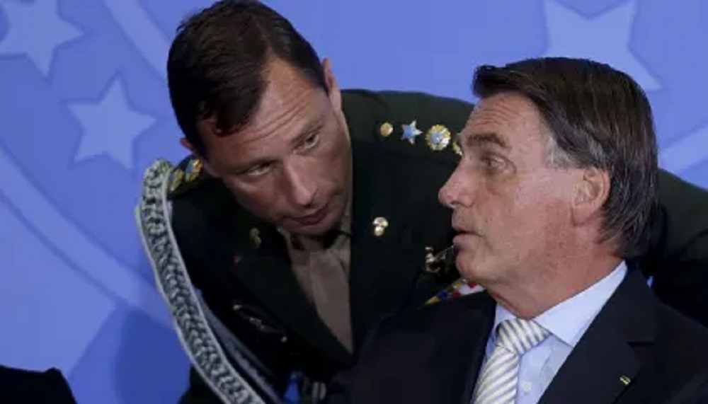 Mauro Cid abaixado e falando com Jair Bolsonaro, que aparece de perfil
