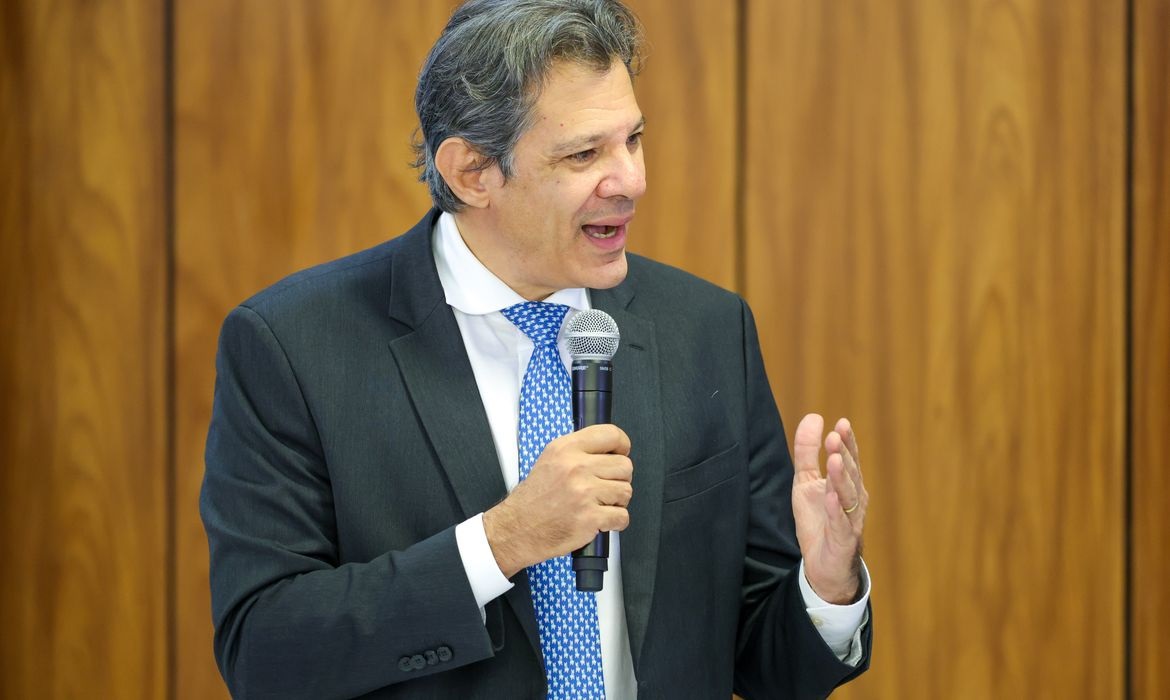 O ministro da Fazenda, Fernando Haddad, de terno e gravata, segurando microfone e falando