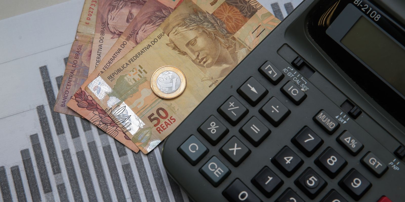 Cédulas de reais e moeda perto de calculadora