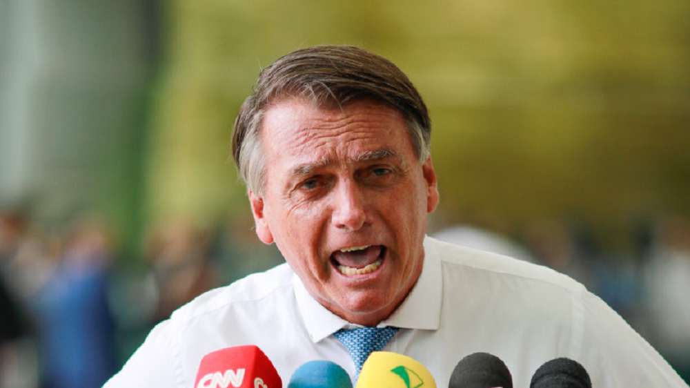 ex-presidente Jair Bolsonaro (PL) gritando para vários microfones, com camisa social branca e gravata azul