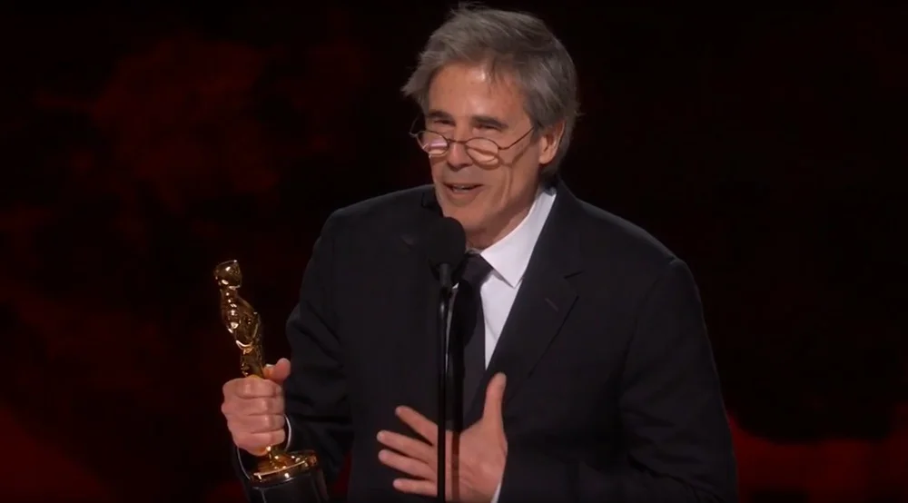 O diretor de Ainda Estou Aqui, Walter Salles, na cerimônia do Oscar 2025, discursando em microfone com estatueta nas mãos