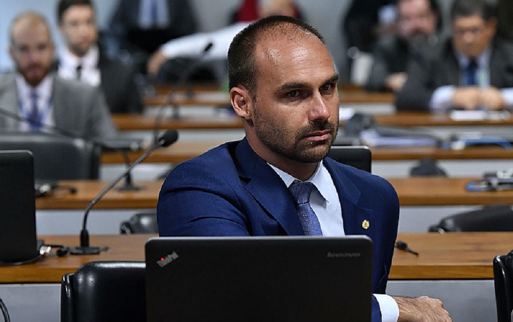 Eduardo Bolsonaro sentado, perto de computador, sério