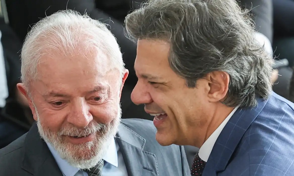 Lula e Haddad com rostos próximos, sorrindo, em close, sem olhar para a câmera