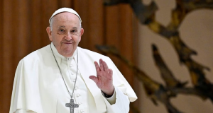 Papa Francisco em pé, acenando, com sorriso tímido, olhando para a câmera