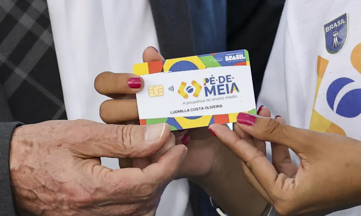 Mão de homem e de mulher segurando cartão do programa Pé-de-Meia