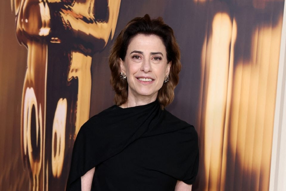 Fernanda Torres olhando para a câmera e sorrindo, de roupa preta e cabelo solto