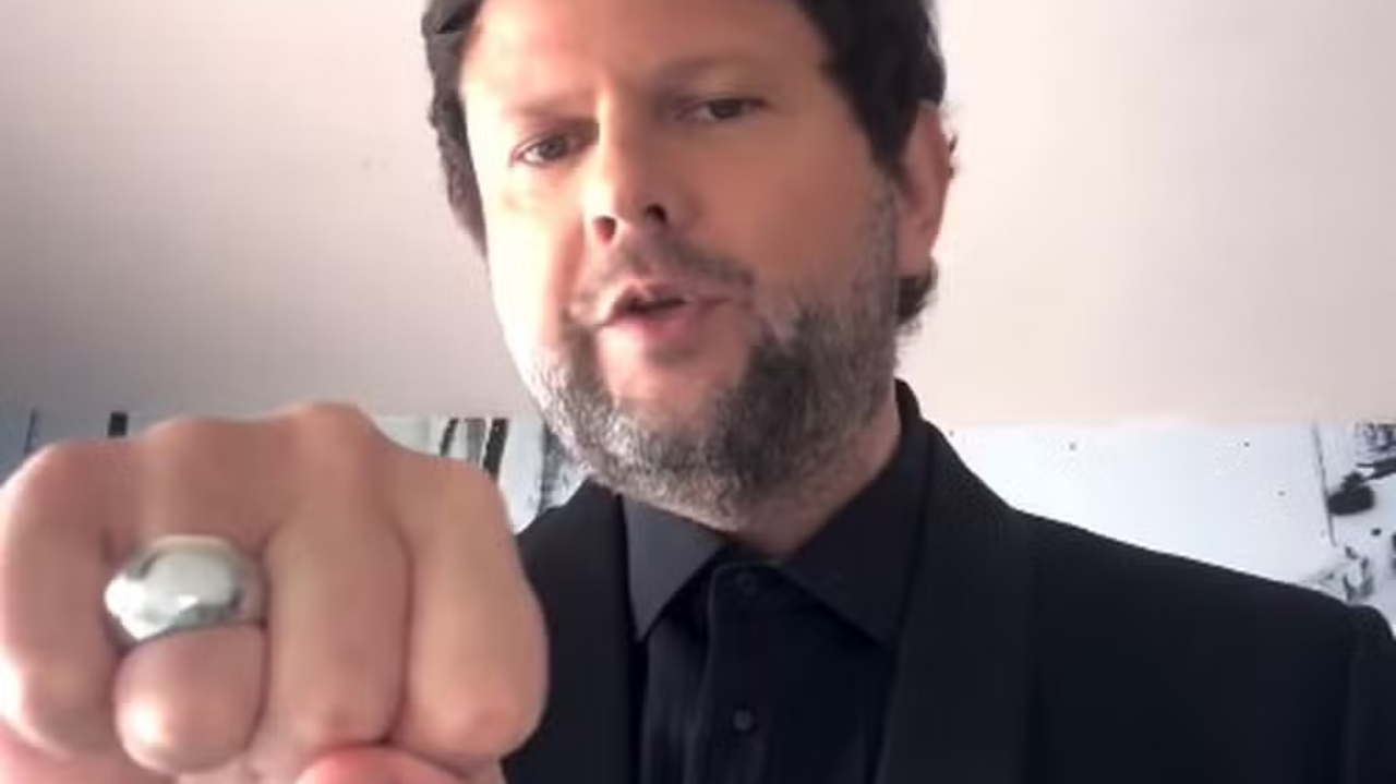 Selton Mello de roupa preta, falando para a câmera e mostrando anel