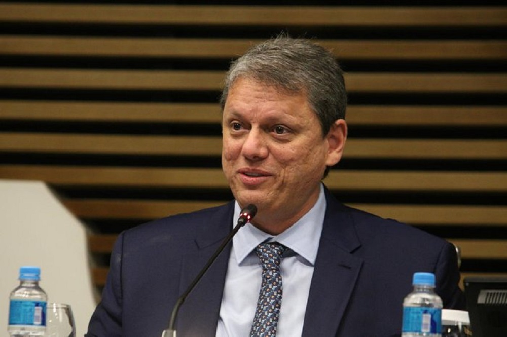 governador Tarcísio de Freitas (Republicanos) com expressão de surpresa e alegria, perto de microfone, sem olhar para a câmera