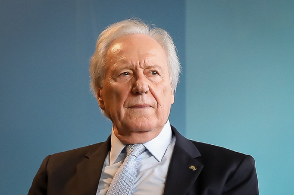 ministro da Justiça e Segurança Pública, Ricardo Lewandowski, olhando para o lado com expressão séria, em fundo azul