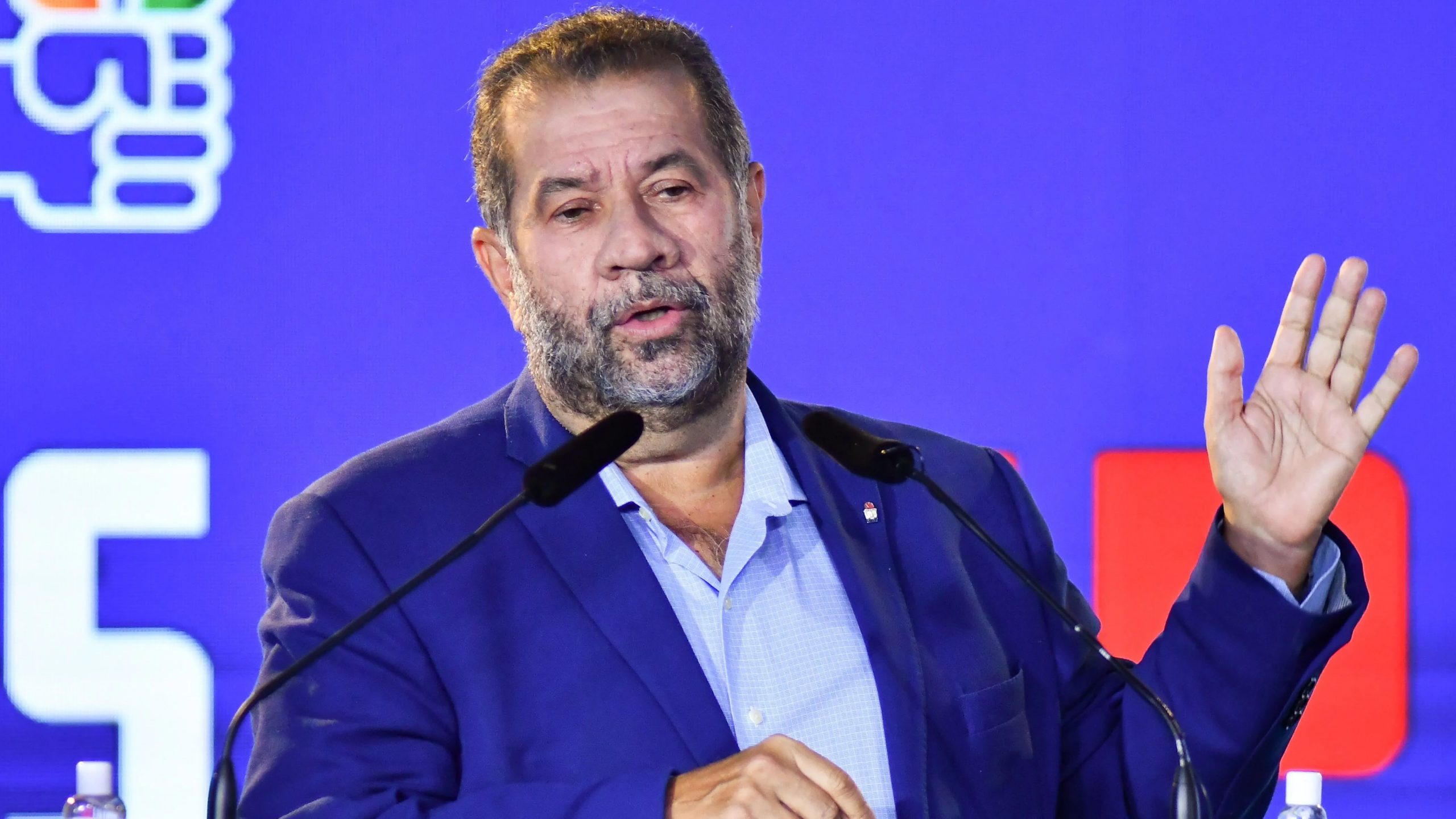 Carlos Lupi de roupa social azul, sério, falando em microfone e gesticulando, sem olhar para a câmera