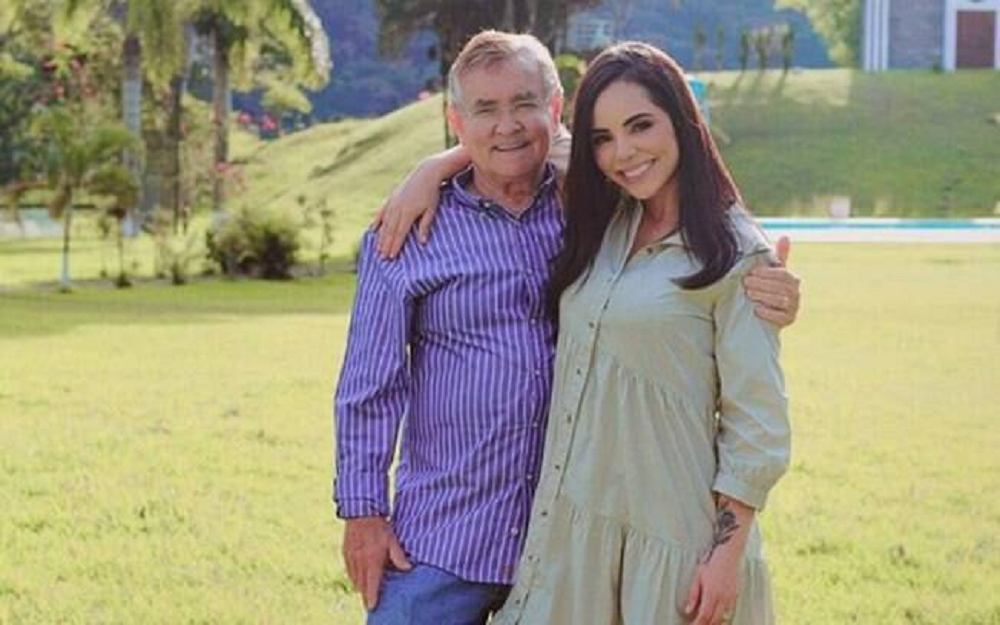 Itamar Serpa e Monique Elias em pé, abraçados, sorrindo para foto em campo aberto