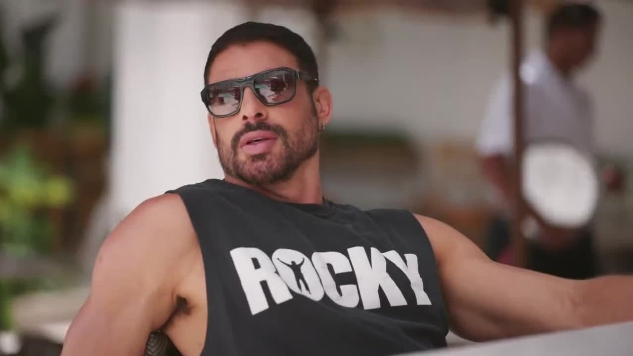 O ator Cauã Reymond de regata preta e óculos escuros, sério, como o César de Vale Tudo