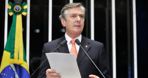 ex-presidente Fernando Collor de Mello falando em microfone, de terno e gravata, com papel na mão, em pé no plenário