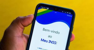 Mão segurando celular aberto na tela inicial do aplicativo Meu INSS