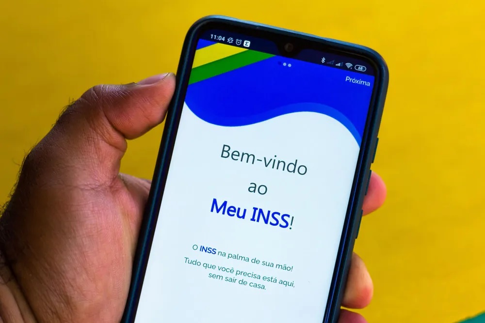 Mão segurando celular aberto na tela inicial do aplicativo Meu INSS