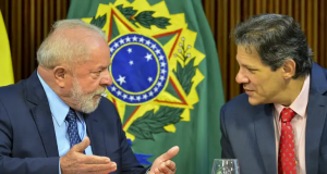 Lula e Haddad conversando, sérios, sentados lado a lado