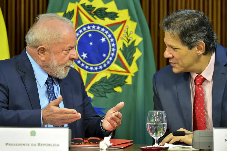 Lula e Haddad conversando, sérios, sentados lado a lado