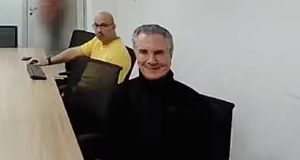 O ex-presidente Fernando Collor de Mello sentado, de roupa preta, sorrindo para a câmera