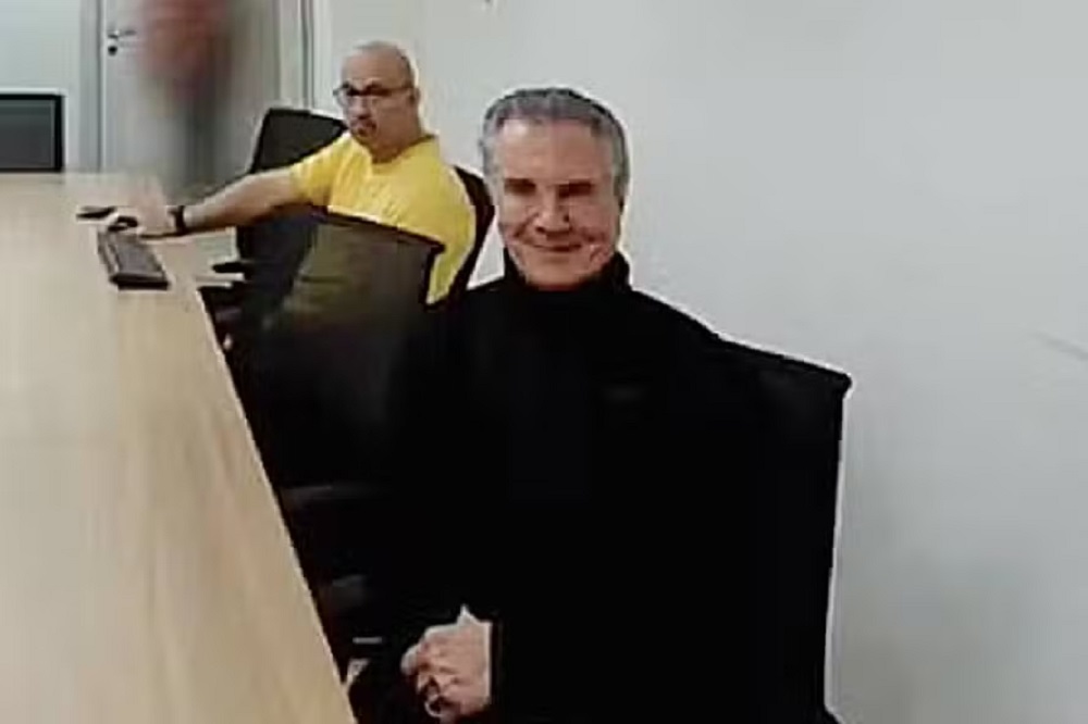 O ex-presidente Fernando Collor de Mello sentado, de roupa preta, sorrindo para a câmera