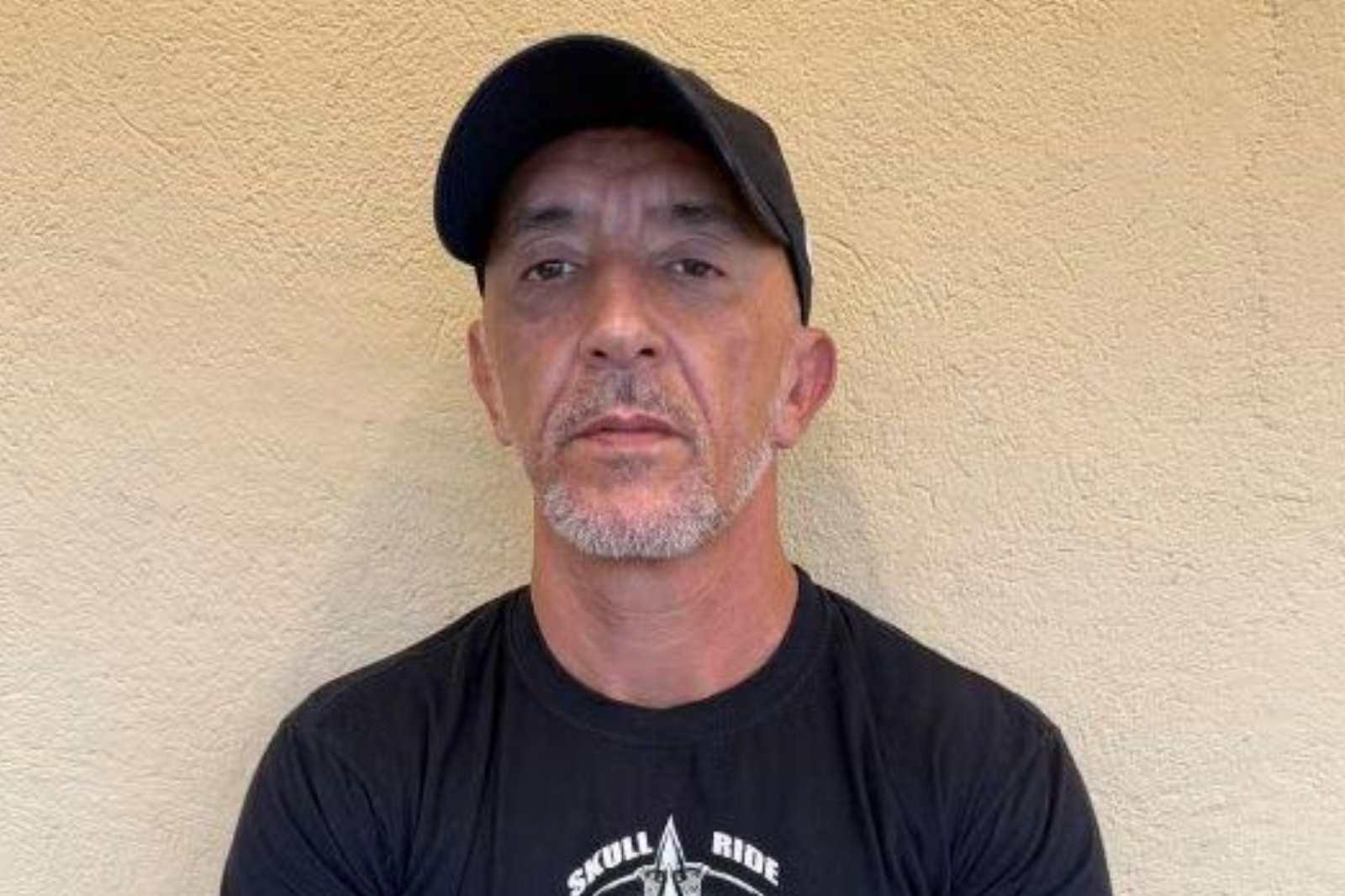 Cristian Cravinhos de boné e camiseta pretos, olhando sério para foto
