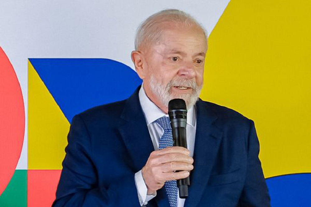 O presidente Luiz Inácio Lula da Silva de terno e gravata, falando em microfone, sem olhar para a câmera