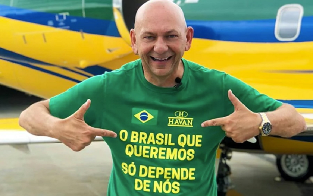 Luciano Hang sorrindo, de camiseta verde, apontando para si mesmo e olhando para a câmera