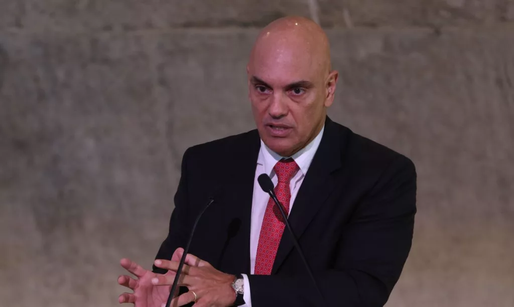 ministro Alexandre de Moraes falando em microfone e gesticulando, sério, sem olhar para a câmera, de roupa social