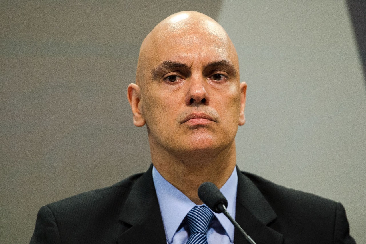 O ministro Alexandre de Moraes, do Supremo Tribunal Federal (STF), com expressão séria, sem olhar para a câmera, sentado perto de microfone