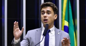 O deputado federal Nikolas Ferreira (PL-MG) de roupa social cinza, falando e gesticulando, sério, no plenário da Câmara dos Deputados