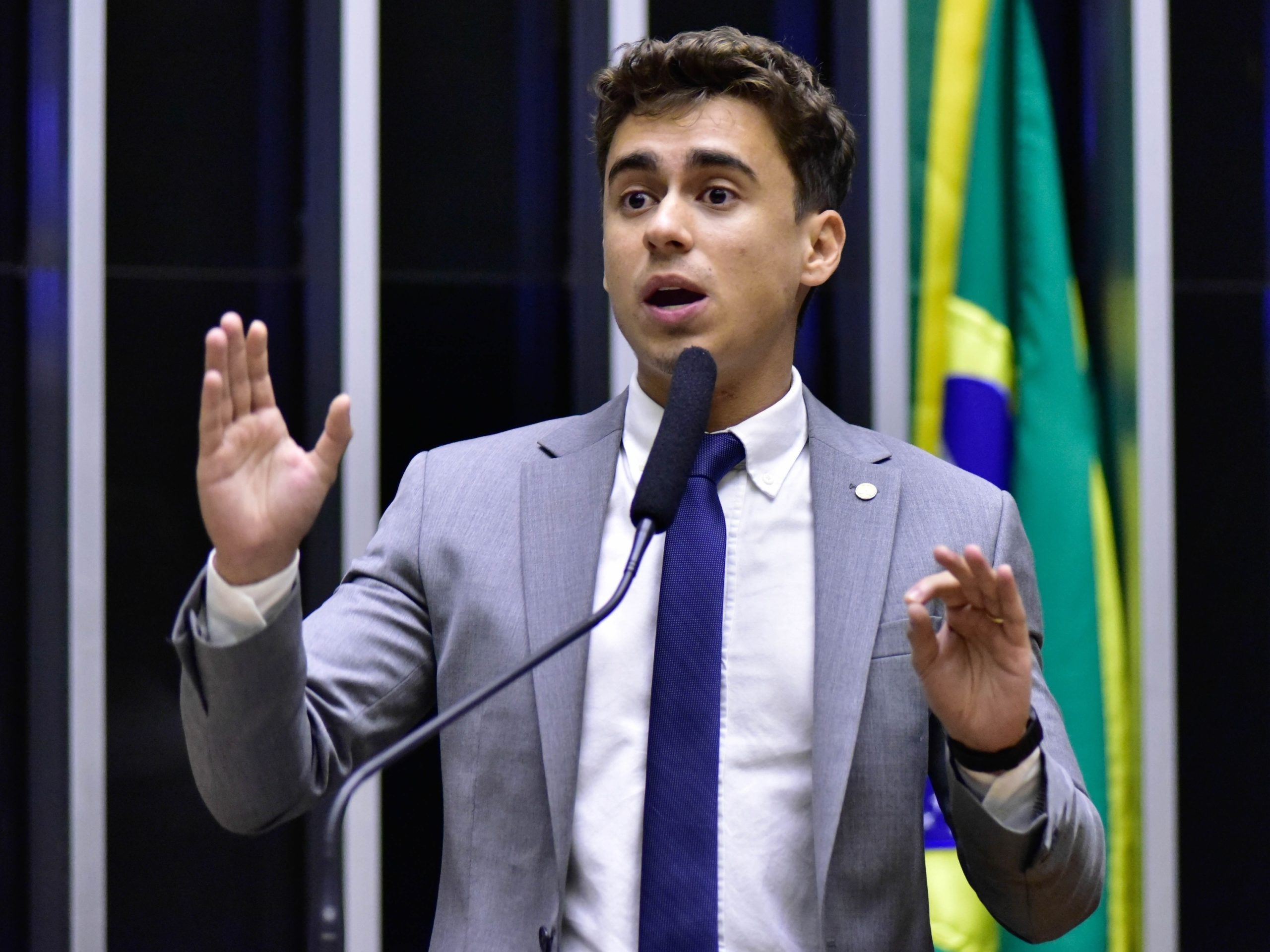 O deputado federal Nikolas Ferreira (PL-MG) de roupa social cinza, falando e gesticulando, sério, no plenário da Câmara dos Deputados