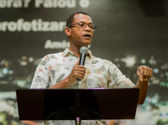 pastor Samuel Bello pregando, segurando microfone, sem olhar para a câmera, sério
