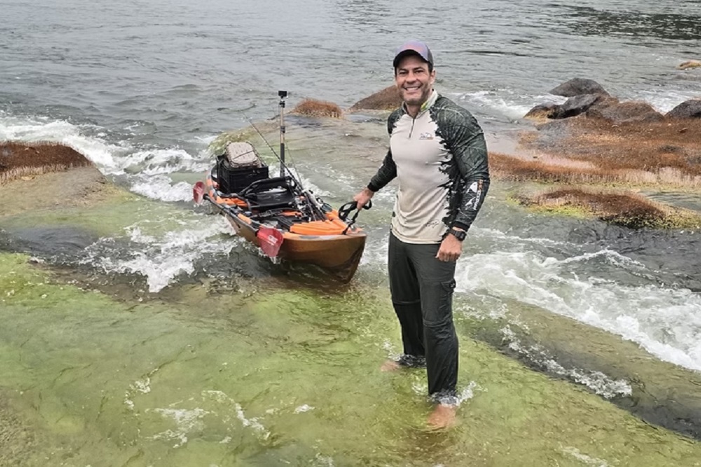 pescador Anderson Guedes em pé na água, sorrindo, de boné