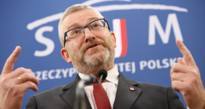 O candidato à presidência polonesa Grzegorz Braun, sério, falando e apontando para cima, de óculos, terno e gravata