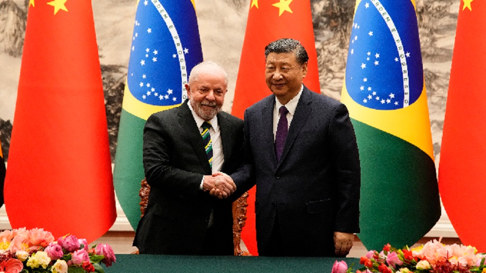 O presidente Lula e o chefe do governo chinês Xi Jinping em aperto de mãos, sorrindo para a câmera
