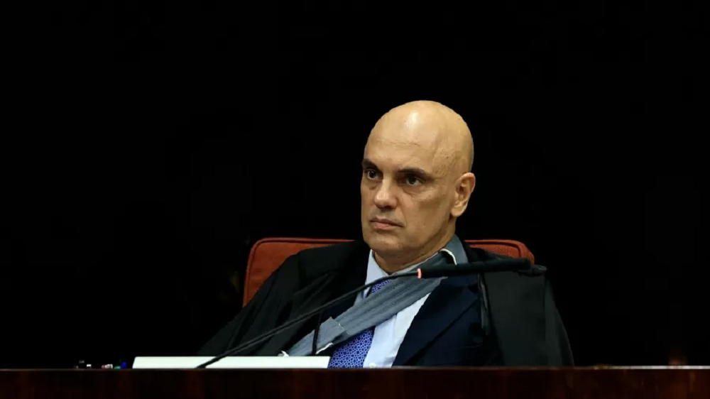 O ministro do STF Alexandre de Moraes olhando para o lado, sério, sentado, de roupa social, perto de microfone