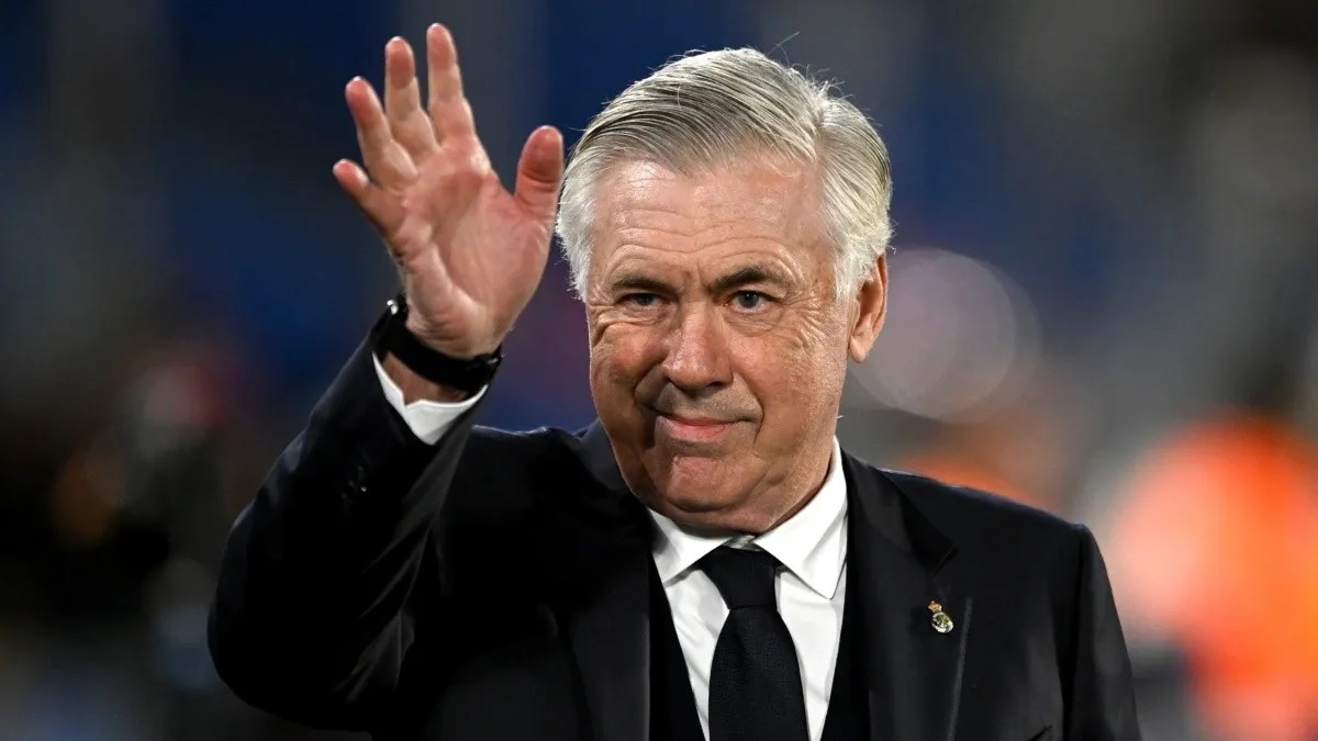 italiano Carlo Ancelotti acenando, com sorriso tímido e roupa social branca e preta