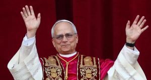 Papa Leão XIV acenando, com sorriso tímido, sem olhar para a câmera