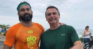 Léo Índio com o ex-presidente Jair Bolsonaro (PL), ambos em pé, lado a lado, sorrindo e fazendo sinal de joia