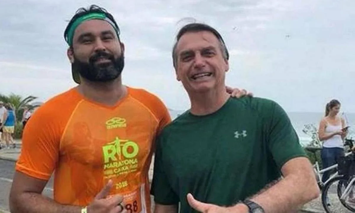 Léo Índio com o ex-presidente Jair Bolsonaro (PL), ambos em pé, lado a lado, sorrindo e fazendo sinal de joia