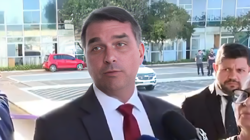 O senador Flávio Bolsonaro (PL-RJ) falando, sério, olhando para o lado, de terno e gravata