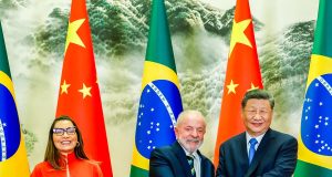 Janja em pé sorrindo e Lula em aperto de mãos com Xi Jinping