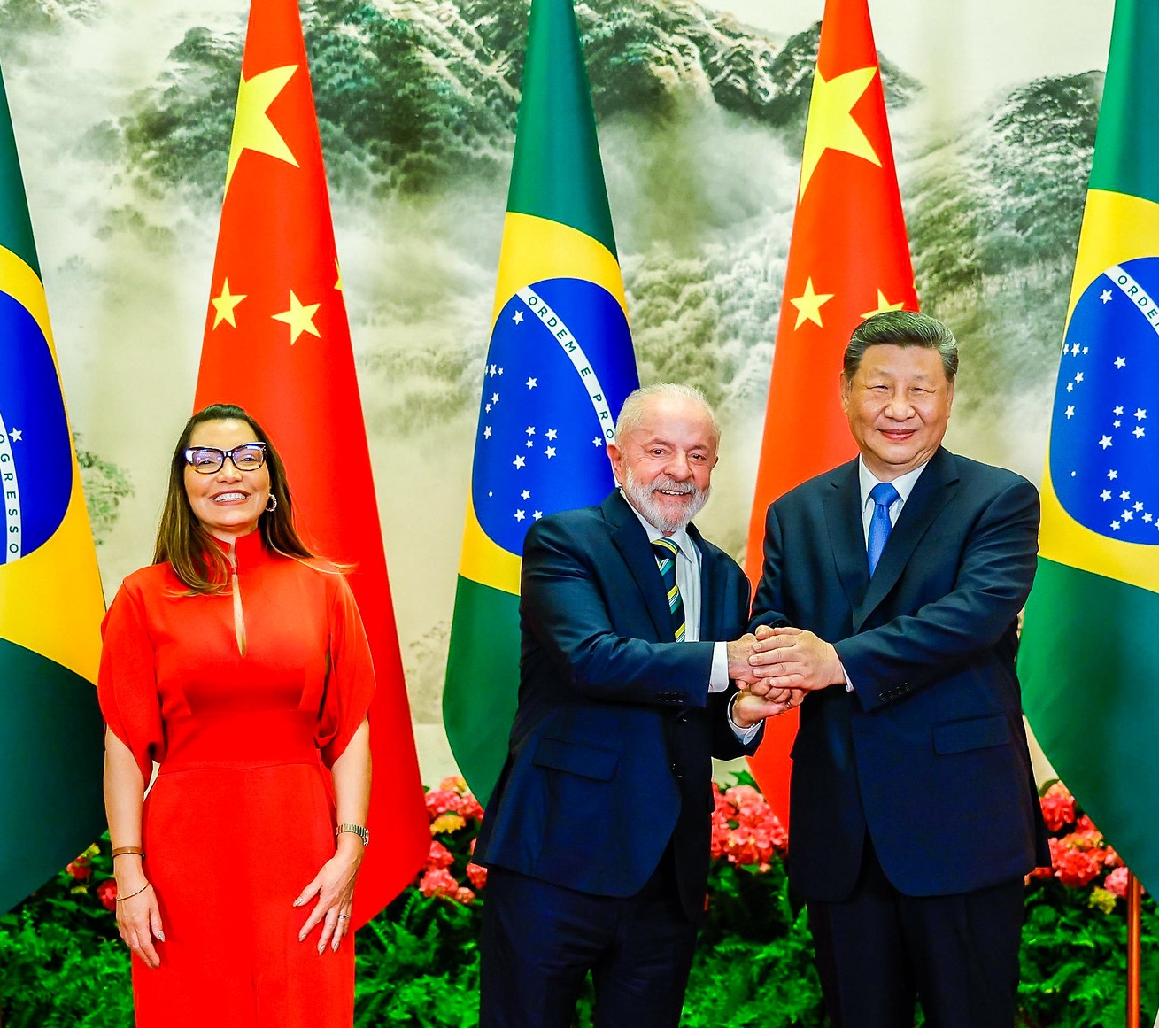 Janja em pé sorrindo e Lula em aperto de mãos com Xi Jinping