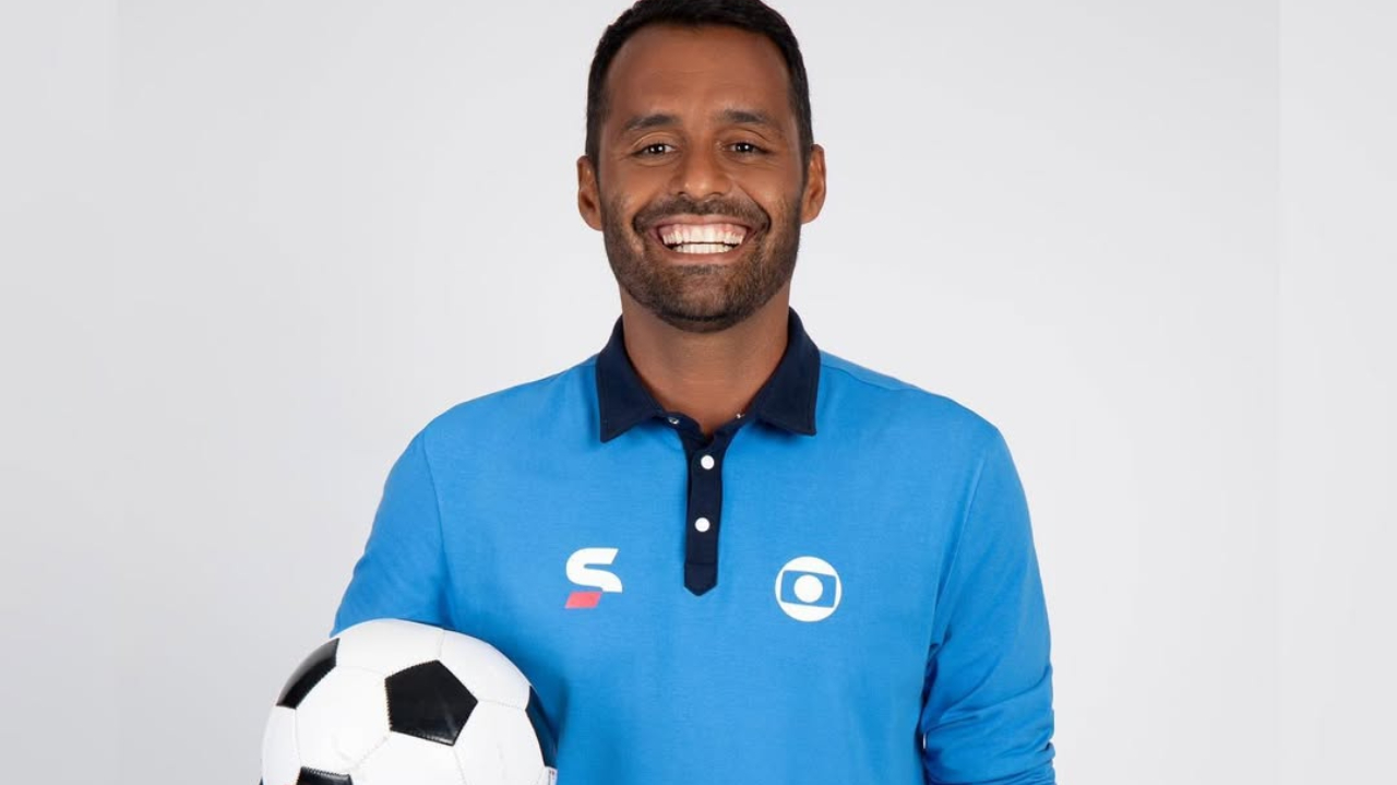Conrado Santana com uniforme do sportv, segurando bola de futebol e sorrindo para a câmera
