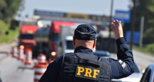 Polícia Rodoviária Federal (PRF) de costas, sinalizando para motoristas
