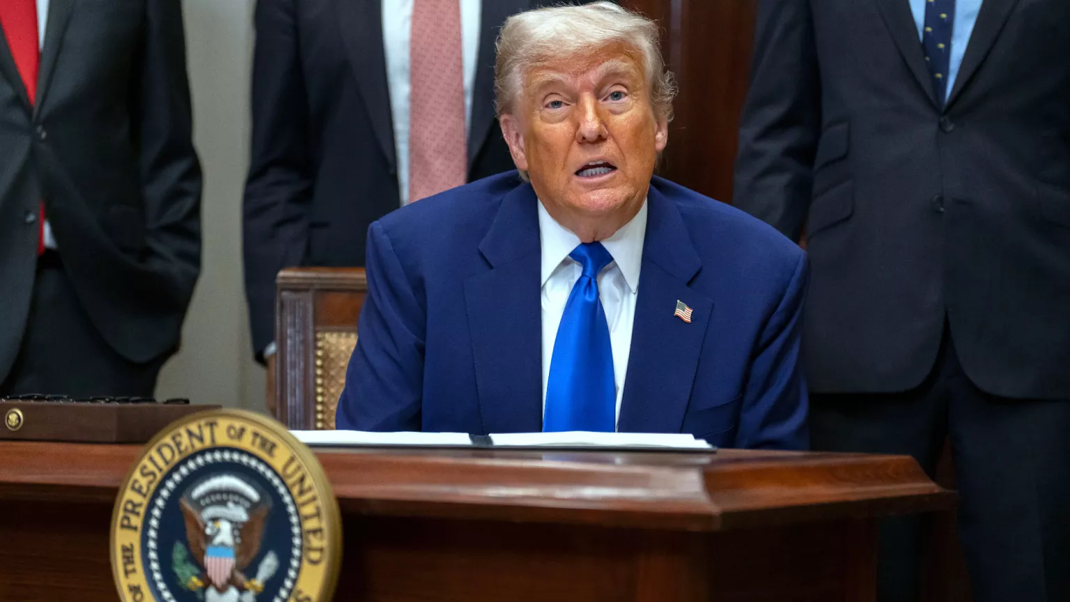 Donald Trump sentado, falando, olhando pra frente, sério