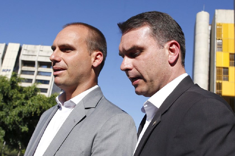 Eduardo Bolsonaro e Flávio, lado a lado, olhando pra frente sem olhar para a câmera, sérios