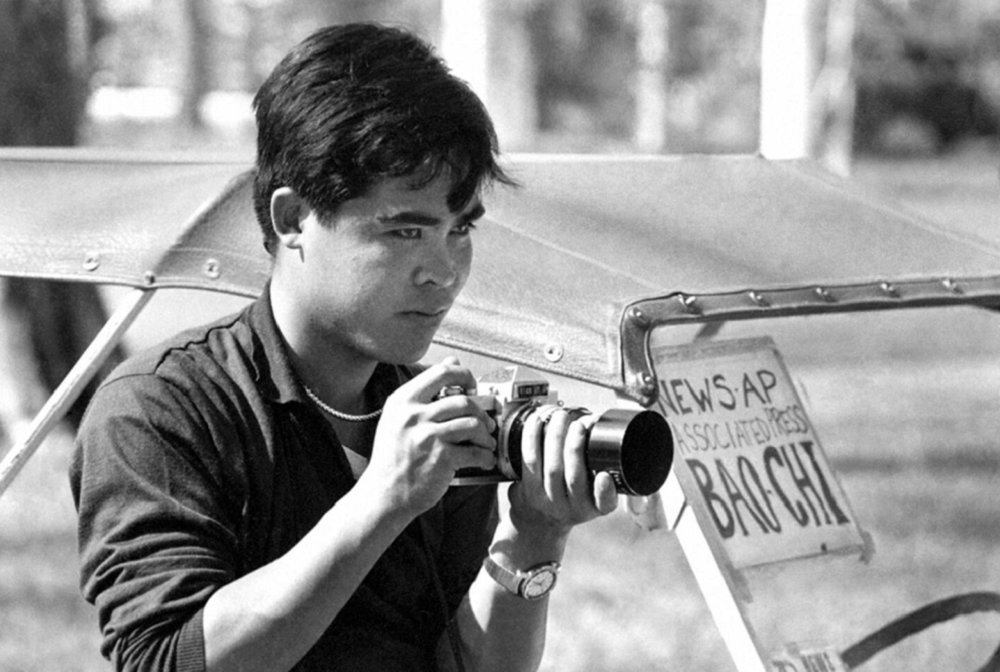 Nick Ut aos 20 anos em foto em preto e branco, com câmera na mão, olhando pra frente, sério