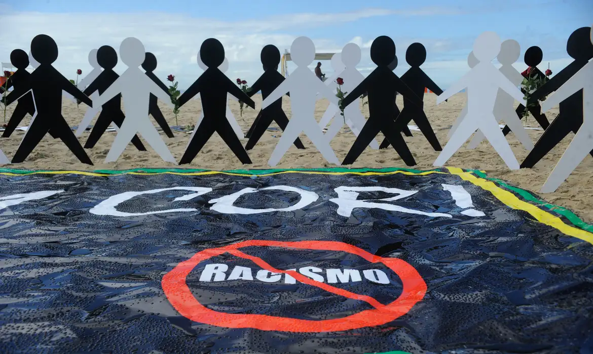 Manifestação contra o racismo na praia com bonecos e faixa