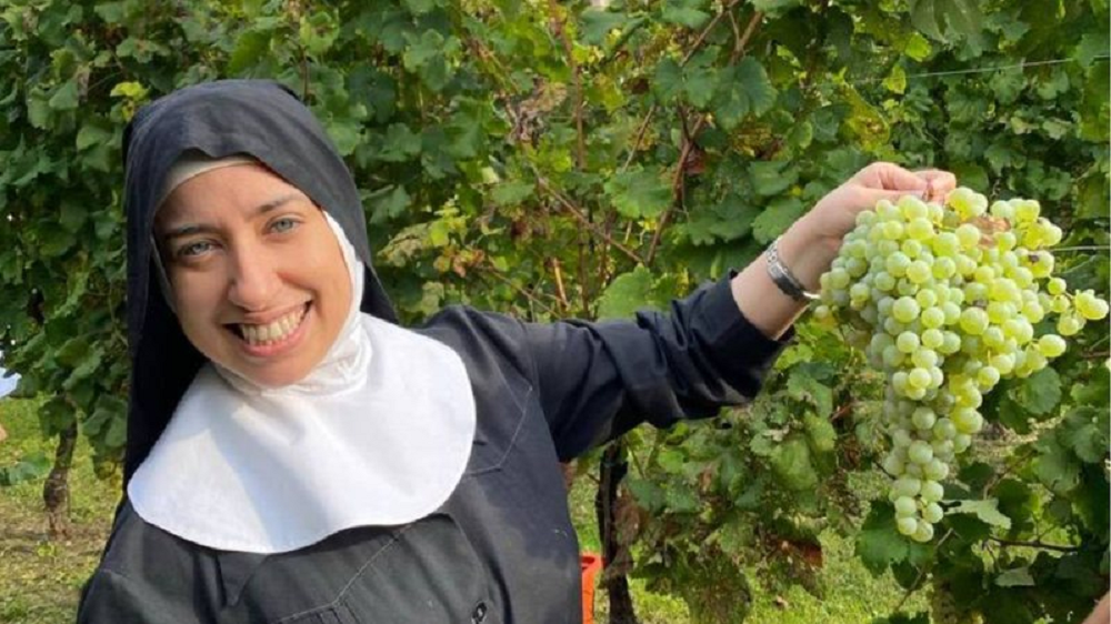 brasileira Aline Pereira Ghammachi vestida como freira posando com cacho de uvas verdes